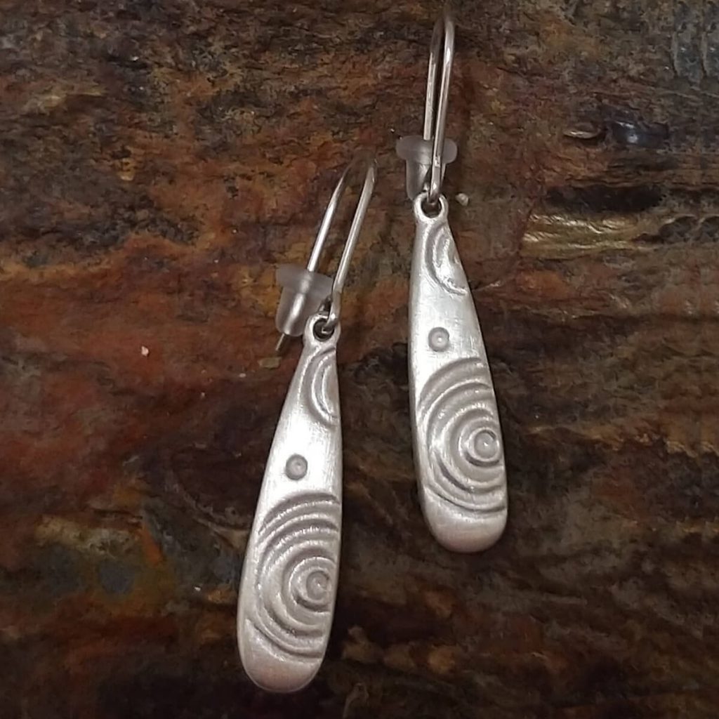 Prehistoric rock art, Ardmore Gallan earrings, sterling silver drop earrings on stone background